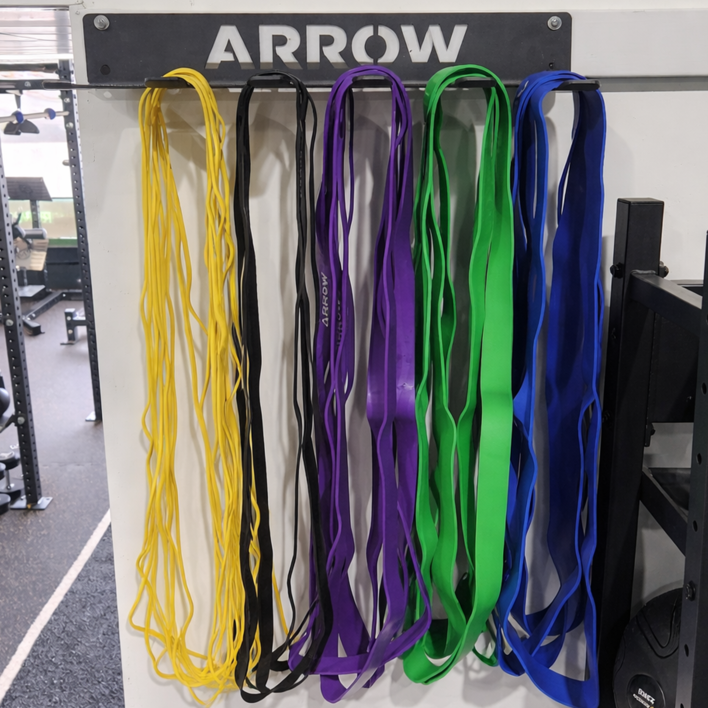 Set of resistance bands in yellow, black, purple, green, and blue hanging on a rack with 'ARROW' branding.