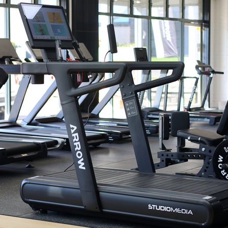 Treadmill with 'Arrow' and 'StudioMedia' branding in a gym setting